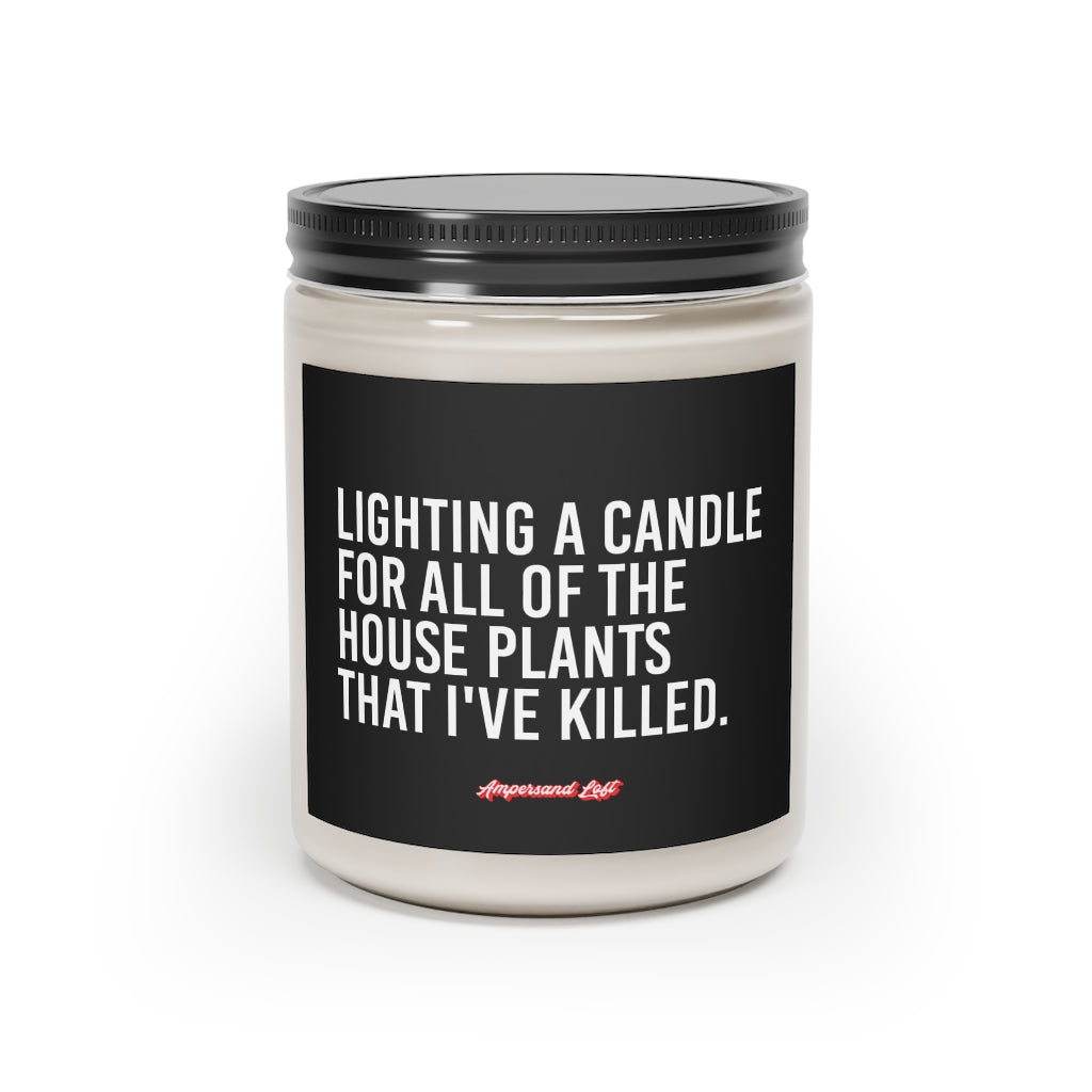 Candle in a glass jar with black label that reads, in white All-Caps text "Lighting a candle for all of the house plants that I've killed." and a small "Ampersand Loft logo below (pink retro font with solid red drop shadow)