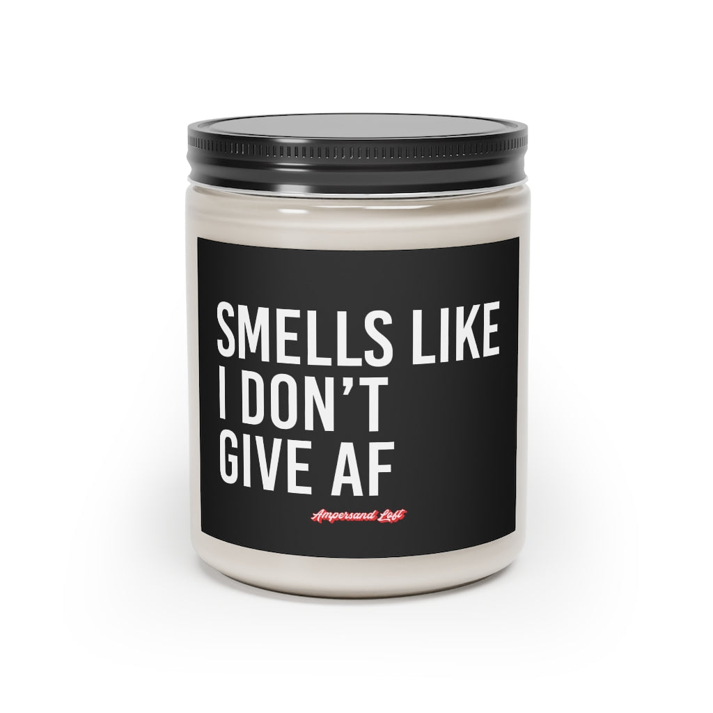 Candle in a glass jar with black label that reads, in white All-Caps text "Smells like I don't give AF." and a small "Ampersand Loft logo below (pink retro font with solid red drop shadow)