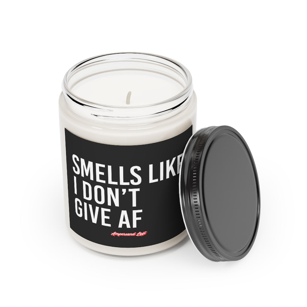 Candle in a glass jar with the lid off, resting on the side of the candle. Black label that reads, in white All-Caps text "Smells like I don't give AF." and a small "Ampersand Loft logo below (pink retro font with solid red drop shadow)
