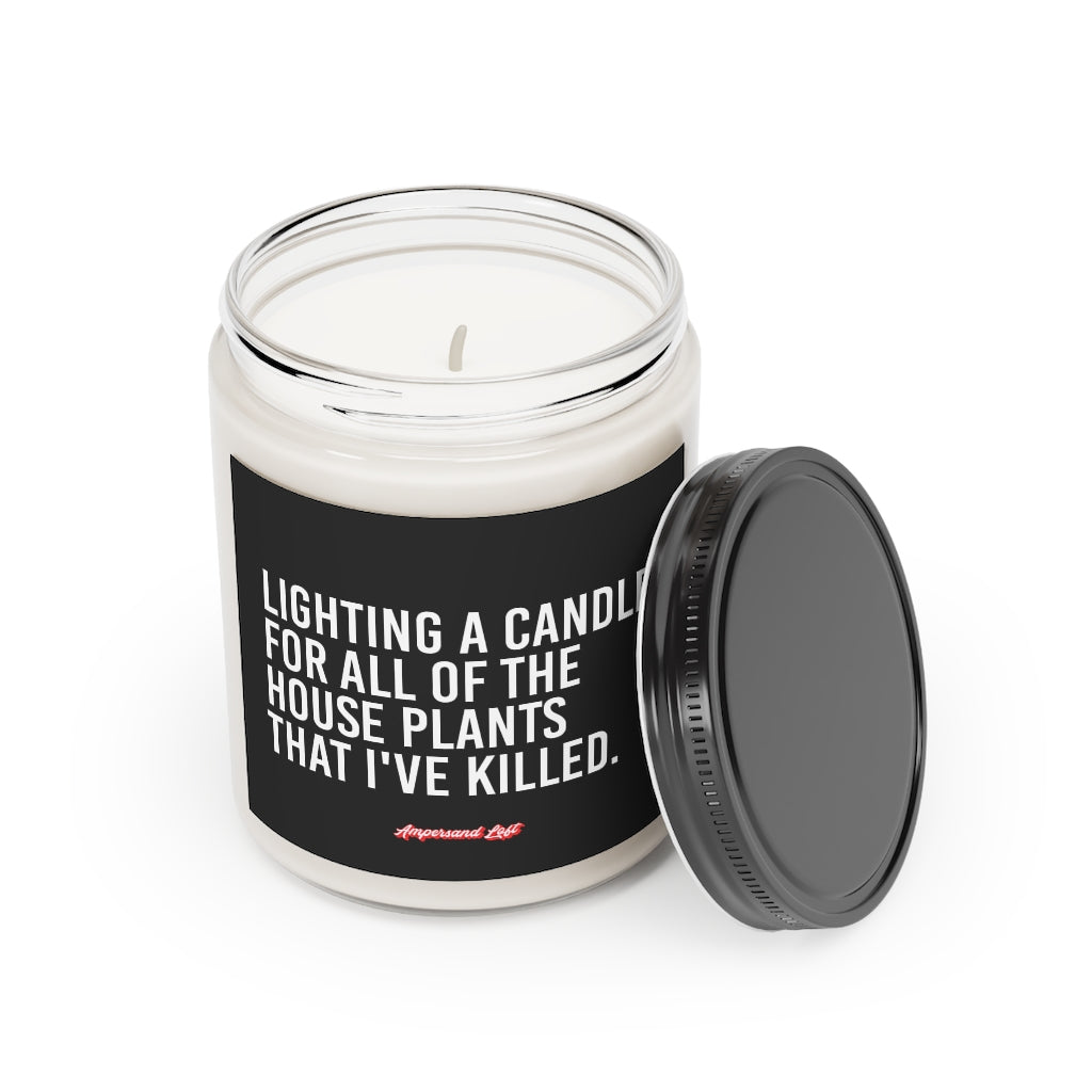 Candle in a glass jar with the lid off, resting on the side of the candle. Black label that reads, in white All-Caps text  "Lighting a candle for all of the house plants that I've killed." and a small "Ampersand Loft logo below (pink retro font with solid red drop shadow)